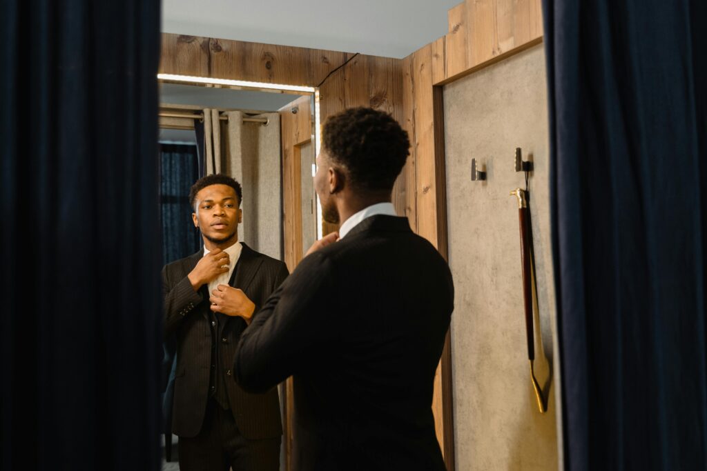 Home Stylish man adjusts his tie in a fitting room mirror, reflecting business confidence.